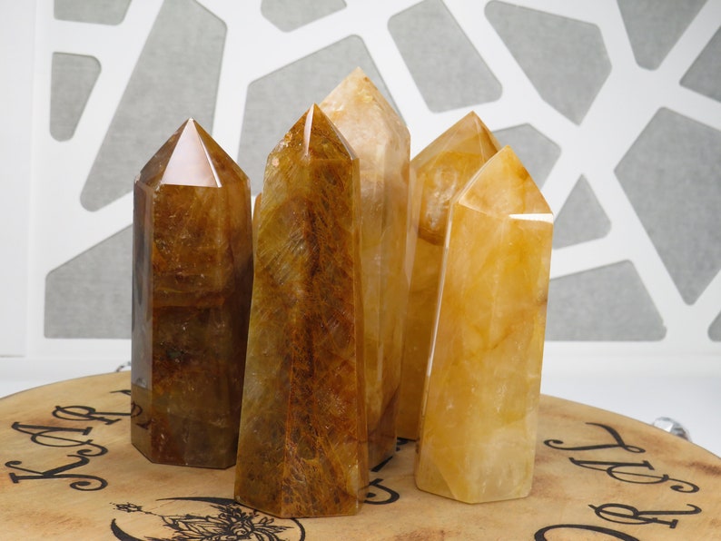 May include: Five golden citrine crystal points arranged on a wooden surface. The points are various sizes and shapes, with some having a more translucent appearance than others.