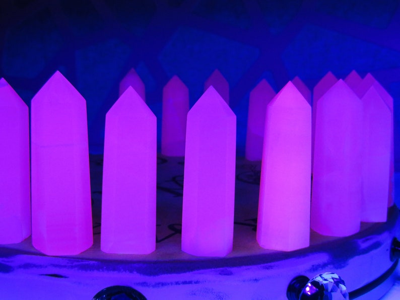 May include: A row of 10 purple crystal points arranged in a circle on a white surface. The crystals are illuminated with a blue light, making them glow.