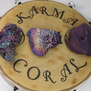 May include: Three iridescent purple and blue Karma Coral stones on a wooden display stand with the words "Karma Coral" engraved on the surface.