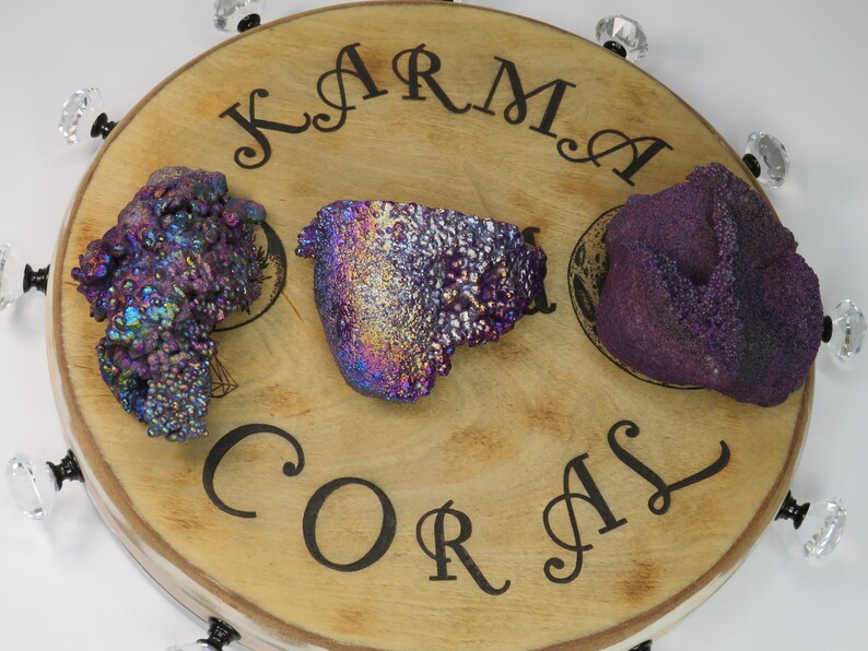 May include: Three iridescent purple and blue Karma Coral stones on a wooden display stand with the words "Karma Coral" engraved on the surface.