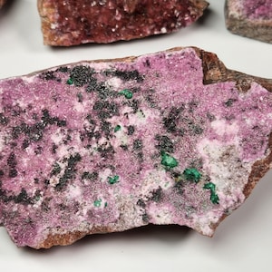 May include: A pink and green mineral specimen with black inclusions. The mineral is rough and has a natural, irregular shape.