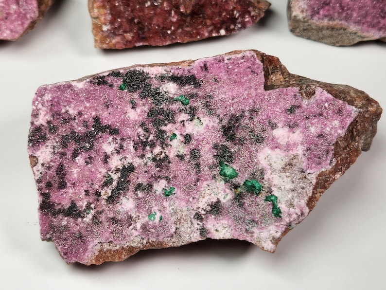 May include: A pink and green mineral specimen with black inclusions. The mineral is rough and has a natural, irregular shape.