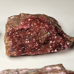 May include: A large, rough, pink and brown rock with a cluster of small, sparkly pink crystals on the surface.