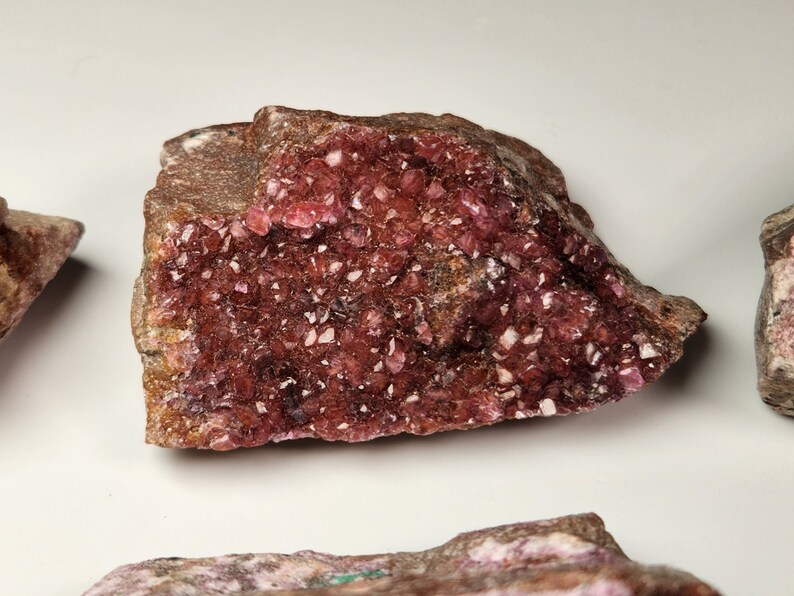May include: A large, rough, pink and brown rock with a cluster of small, sparkly pink crystals on the surface.