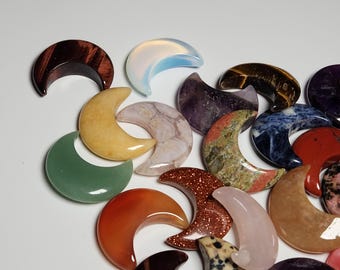 May include: A collection of crescent moon shaped polished stones in various colors, including green, red, orange, yellow, blue, purple, brown, and white.