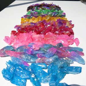May include: A rainbow assortment of iridescent crystal points. The crystals are arranged in a rainbow order, starting with purple and ending with blue.