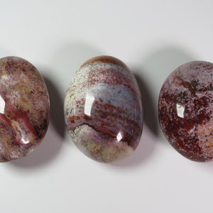 May include: Three smooth, polished, oval-shaped stones with a red, white and grey marbled pattern.