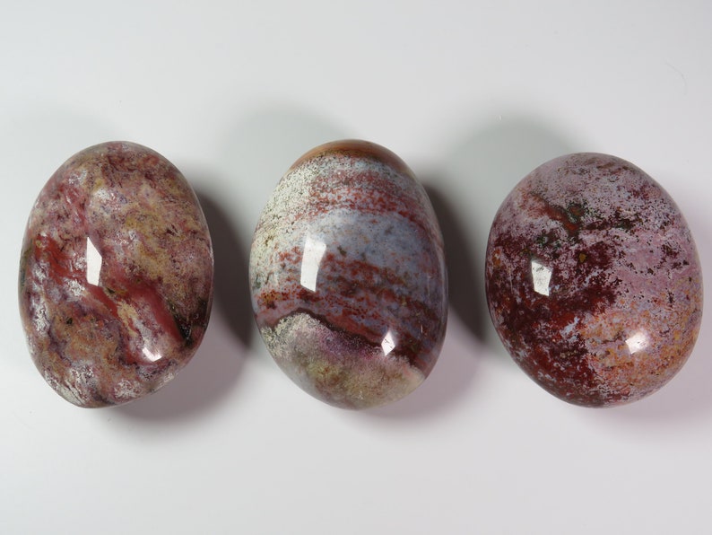 May include: Three smooth, polished, oval-shaped stones with a red, white and grey marbled pattern.