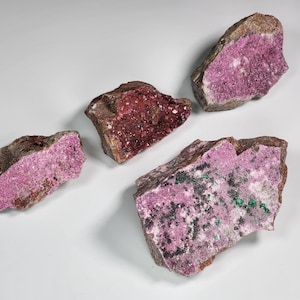 May include: Four rough, irregularly shaped pieces of pink and green cobalt calcite. The mineral has a crystalline texture and is a popular choice for collectors.
