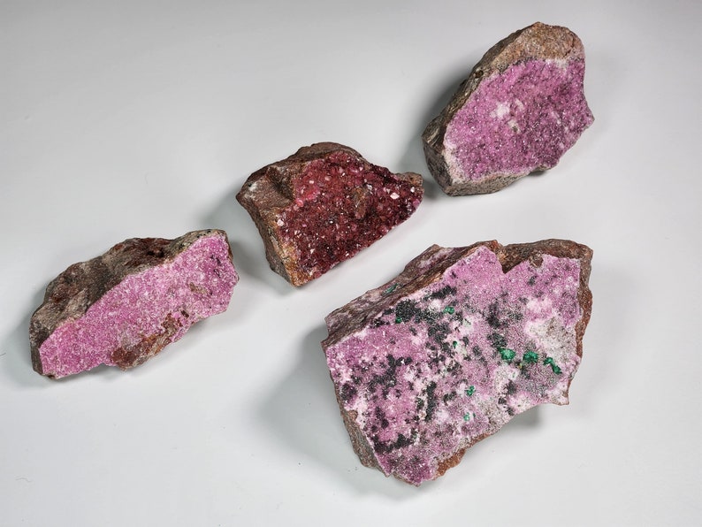 May include: Four rough, irregularly shaped pieces of pink and green cobalt calcite. The mineral has a crystalline texture and is a popular choice for collectors.