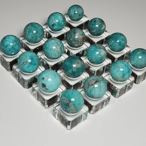 May include: Twenty teal green spheres of amazonite, each displayed on a clear glass pedestal. The spheres are arranged in a grid pattern.