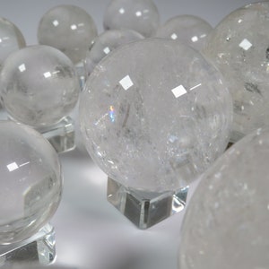 May include: A group of clear quartz crystal spheres on display stands. The spheres are various sizes and have a translucent, glassy appearance.