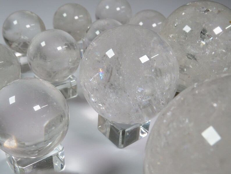 May include: A group of clear quartz crystal spheres on display stands. The spheres are various sizes and have a translucent, glassy appearance.