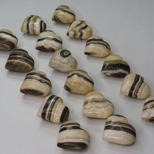 May include: A collection of 18 heart-shaped polished stones with brown and white stripes. The stones are arranged in a row on a white surface.