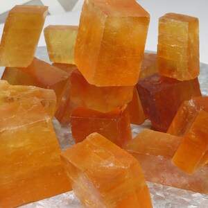 Può includere: Una collezione di cristalli di calcite arancioni, alcuni dei quali sono impilati uno sopra l'altro, su un vassoio d'argento.