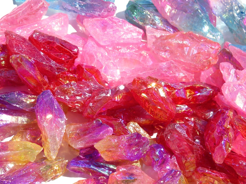 May include: A collection of iridescent quartz crystals in various shades of pink, red, and purple. The crystals are raw and have a natural, rough texture.