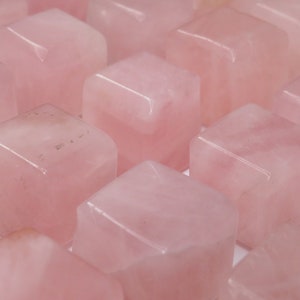 May include: A collection of pink rose quartz tumbled stones in a cube shape. The stones are smooth and polished.