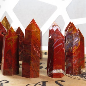 May include: A group of ten red, orange, and white banded agate crystal points. The points are arranged in a semi-circle on a brown surface with a black and white design.