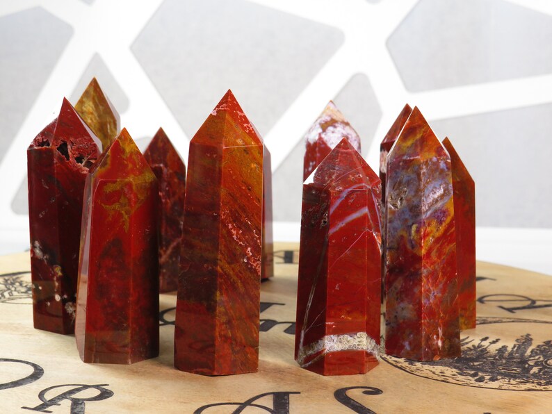 May include: A group of ten red, orange, and white banded agate crystal points. The points are arranged in a semi-circle on a brown surface with a black and white design.