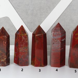 May include: Five red jasper crystal points, numbered 1 through 5, arranged in a row on a white surface.