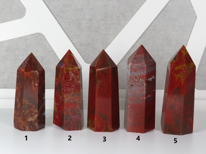 May include: Five red jasper crystal points, numbered 1 through 5, arranged in a row on a white surface.