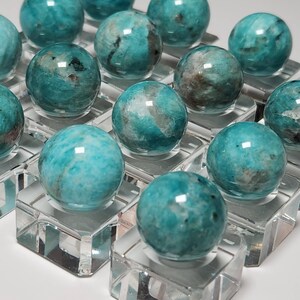 May include: A collection of 14 teal green amazonite spheres displayed on clear acrylic stands. The spheres are polished and have a smooth, glassy finish.
