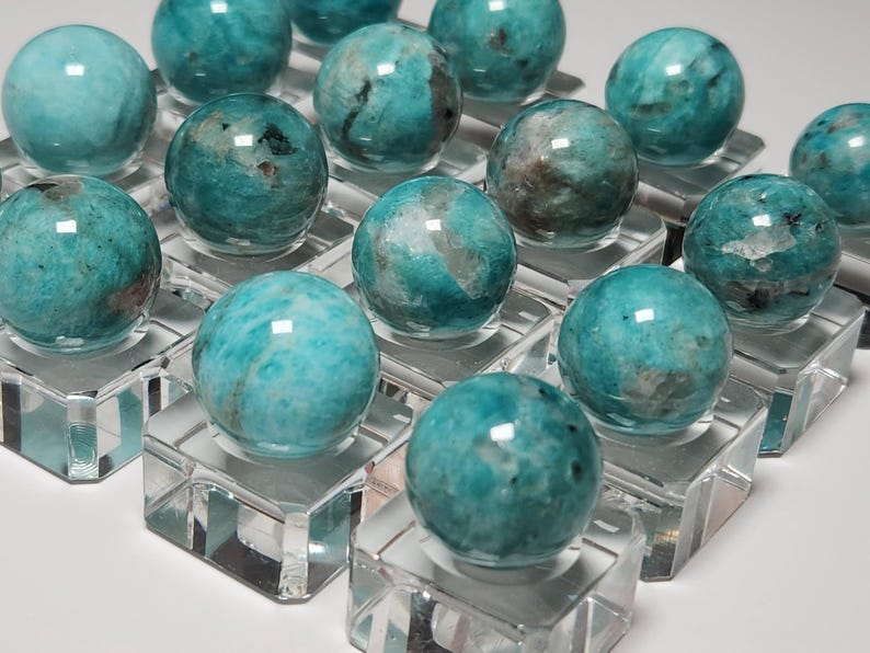 May include: A collection of 14 teal green amazonite spheres displayed on clear acrylic stands. The spheres are polished and have a smooth, glassy finish.