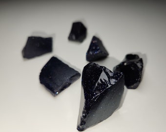 Puede incluir: Una colección de seis piezas de piedras preciosas de color azul oscuro, brillantes y talladas en bruto, sobre una superficie blanca.