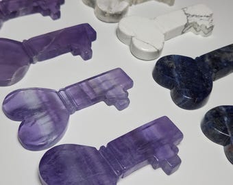 Op de afbeelding: Een set van zeven hartvormige, sleutel-vormige kristallen ornamenten in paars, blauw en wit.