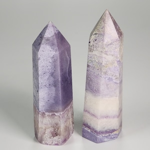 May include: Two purple and white fluorite crystal points. The crystals are both pointed and have a hexagonal base.