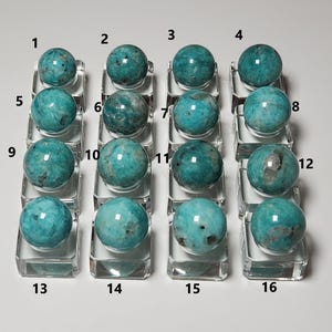 May include: A collection of 16 teal green amazonite spheres displayed on clear glass bases. The spheres are numbered 1 through 16.