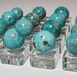 May include: A collection of 15 teal green amazonite spheres on clear glass display stands. The spheres are polished and have a natural, cloudy appearance.