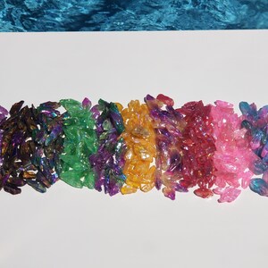 May include: A rainbow assortment of iridescent crystal chips. The chips are arranged in a row, with each colour blending into the next. The colours are purple, green, blue, orange, red, pink, and blue.