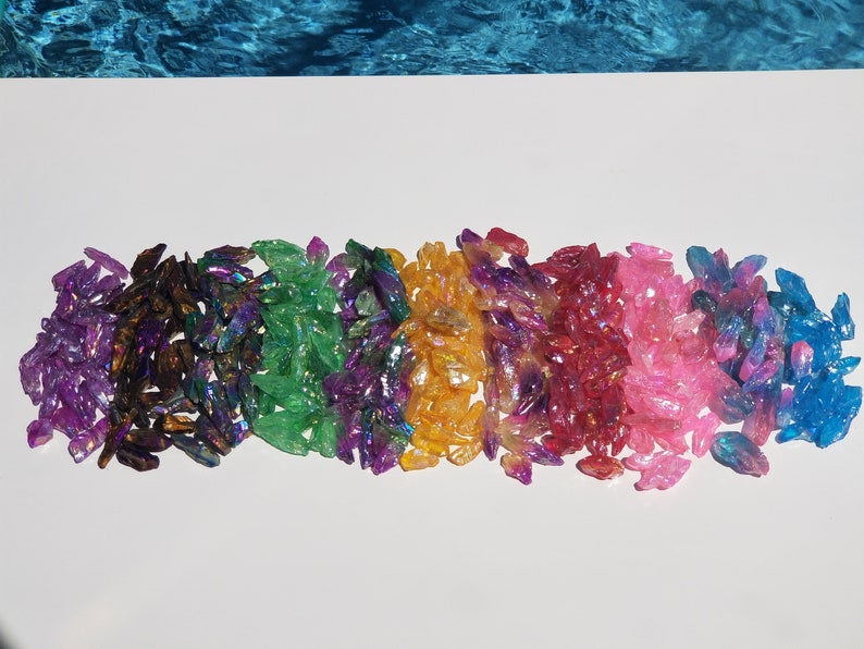 May include: A rainbow assortment of iridescent crystal chips. The chips are arranged in a row, with each colour blending into the next. The colours are purple, green, blue, orange, red, pink, and blue.