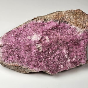 May include: A pink and gray rock with a large, flat surface covered in small, sparkly pink crystals.