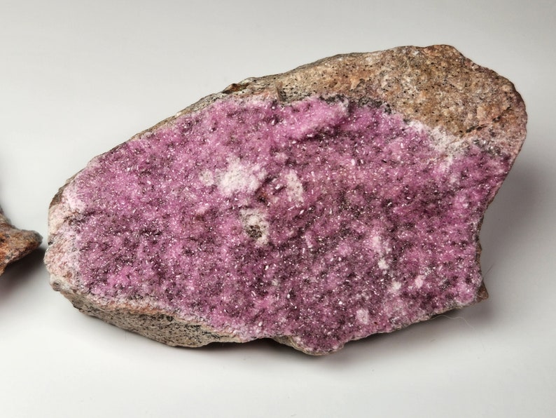 May include: A pink and gray rock with a large, flat surface covered in small, sparkly pink crystals.