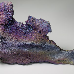 May include: A large, iridescent, purple and blue mineral specimen with a rough, textured surface. The mineral has a unique, organic shape and appears to be made of many small crystals.
