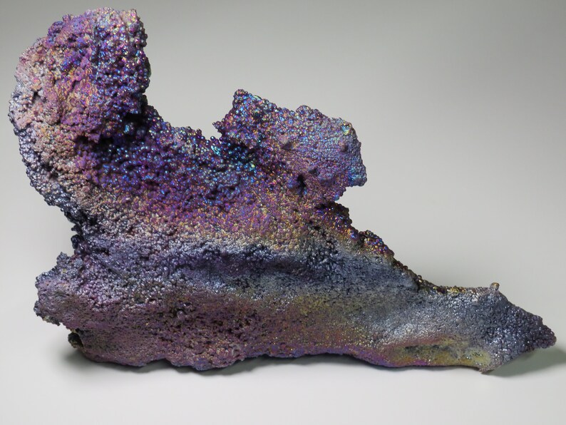 May include: A large, iridescent, purple and blue mineral specimen with a rough, textured surface. The mineral has a unique, organic shape and appears to be made of many small crystals.