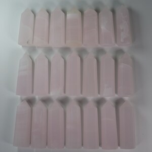 May include: A collection of 30 pink selenite crystal points arranged in three rows of ten. The points are all approximately the same size and shape, and they have a smooth, polished finish.