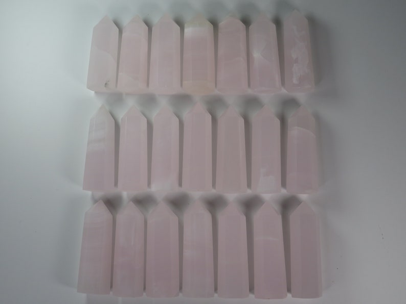 May include: A collection of 30 pink selenite crystal points arranged in three rows of ten. The points are all approximately the same size and shape, and they have a smooth, polished finish.