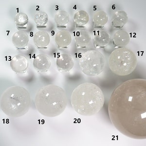 May include: Twenty-one clear quartz crystal spheres of varying sizes, displayed on a white surface. The spheres are numbered 1 through 21.