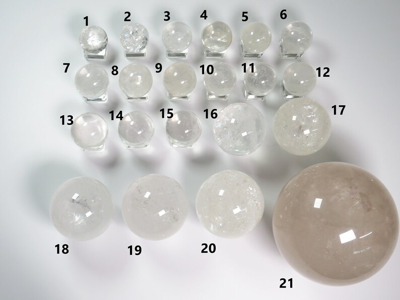 May include: Twenty-one clear quartz crystal spheres of varying sizes, displayed on a white surface. The spheres are numbered 1 through 21.