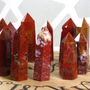 May include: A group of ten red, brown, and white jasper crystal points. The points are arranged in a circle on a wooden surface.