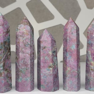 May include: Six pink and green gemstone points, also known as rubellite, are arranged in a row on a gray background. The points are all different sizes and have a variety of patterns.