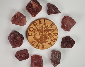 以下が含まれることがあります： 木製の円形に「Coral Karma And」と刻まれた文字が書かれた、11個の赤褐色のクリスタルストーンの集まり。一部はわずかにピンクがかった色合いをしています。