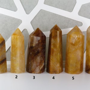 May include: Six yellow and brown crystal points, numbered 1 through 6, arranged in a row on a white surface.
