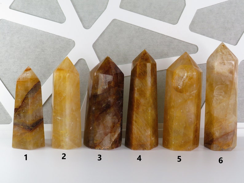 May include: Six yellow and brown crystal points, numbered 1 through 6, arranged in a row on a white surface.