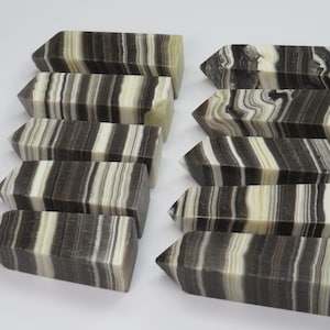 May include: Ten black and white striped crystal points, also known as banded onyx, arranged in two rows. The points are polished and have a smooth, glossy finish.