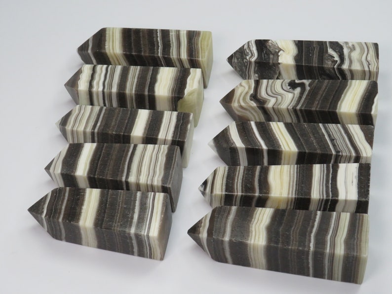 May include: Ten black and white striped crystal points, also known as banded onyx, arranged in two rows. The points are polished and have a smooth, glossy finish.