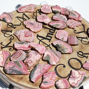 May include: A round wooden board with the names "Kara & Andrew" engraved on it. The board is decorated with pink and grey banded agate slices.